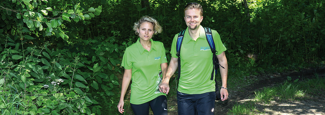 Auf einem schattigen Waldweg wandert ein Paar Händchenhaltend und glücklich.